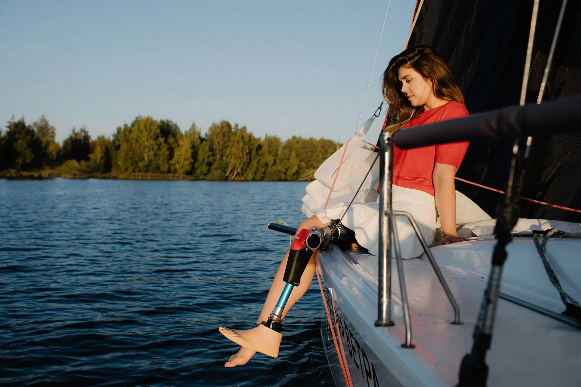 Woman sitting on the edge of a boat on the lake, with a leg prosthesis and a carbon foot