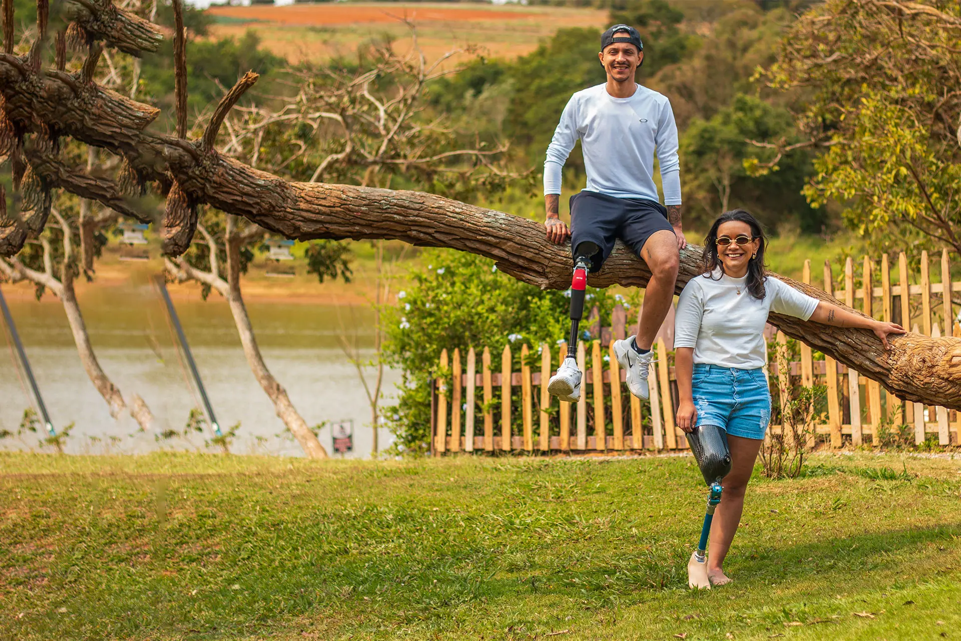 Man and woman with leg prostheses sitting on a log by the lake