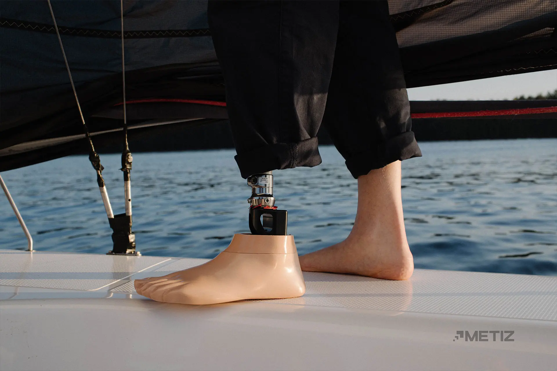 Prosthetic foot resting on the deck of a boat, next to a bare foot, with water in the background